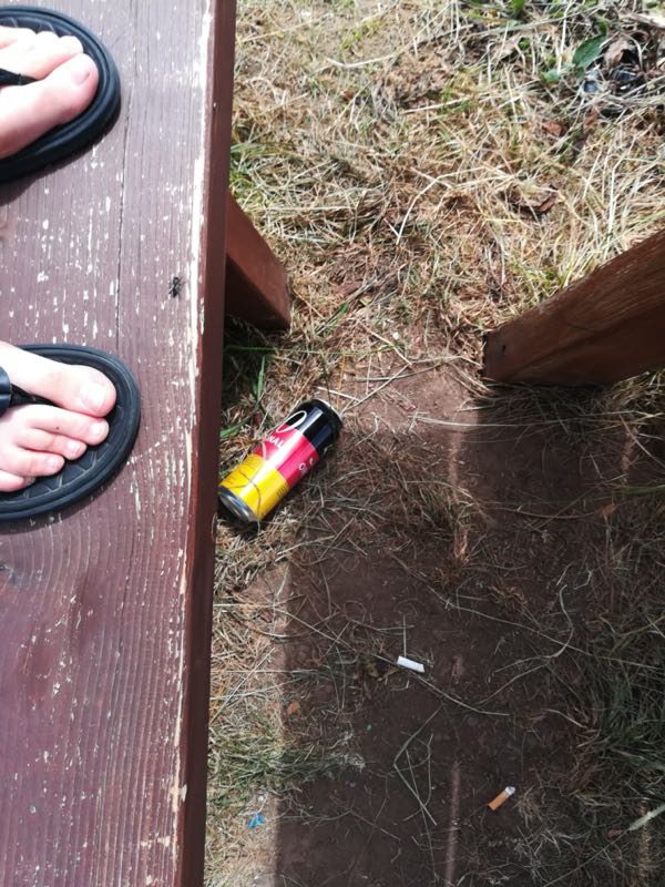 Nackte Füße in Flip-Flops stehen auf einer Bank. Auf dem Boden liegt eine Bierdose. 